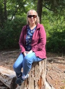 Photograph of Linda Thomas sitting on a cut tree trunk in the woods